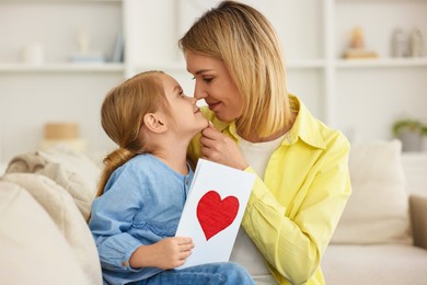 Photo of Little daughter congratulating her mom with greeting card at home. Happy Mother's Day