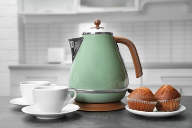 Photo of Modern electric kettle, cups and muffins on grey table in kitchen