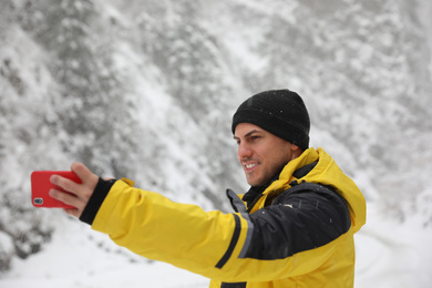 Handsome man taking selfie outdoors on snowy day. Winter vacation