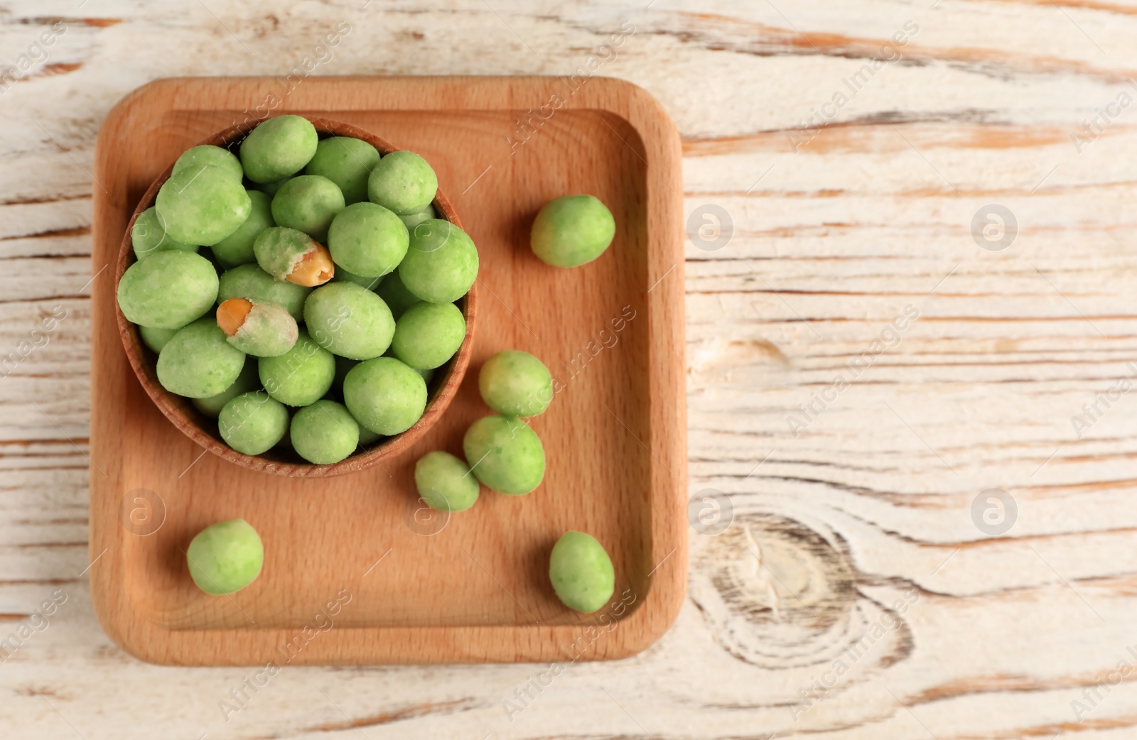 Photo of Tasty wasabi coated peanuts on white wooden table, top view. Space for text