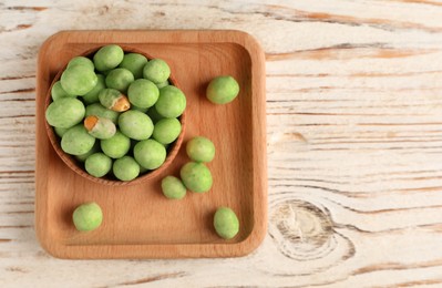Photo of Tasty wasabi coated peanuts on white wooden table, top view. Space for text