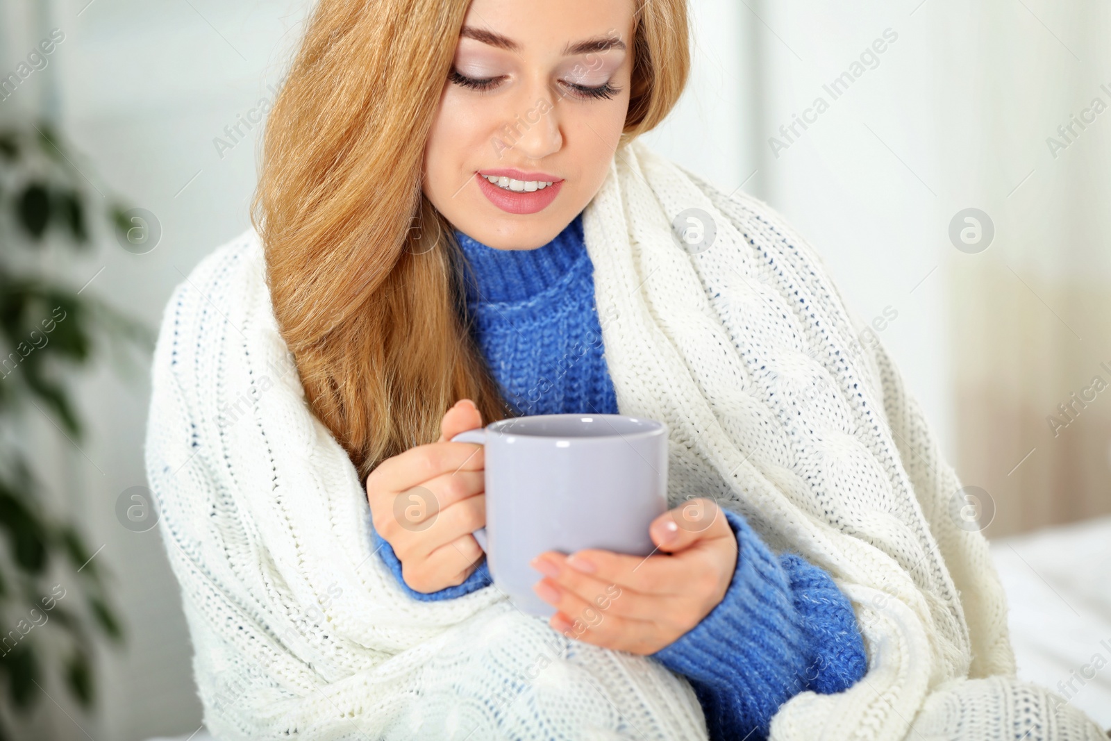 Photo of Attractive young woman in cozy warm sweater with cup of hot drink and plaid at home