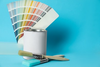 Photo of Can of paint, color palette samples and brushes on turquoise background. Space for text