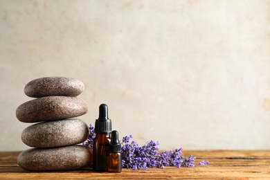 Photo of Bottles of essential oil, spa stones and lavender flowers on wooden table. Space for text