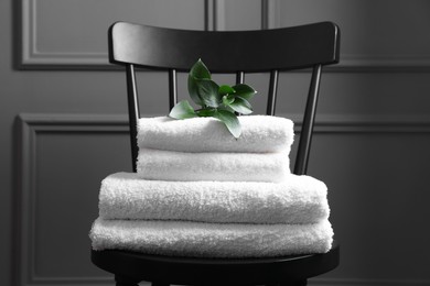 Photo of Stacked soft towels and green leaves on black chair indoors