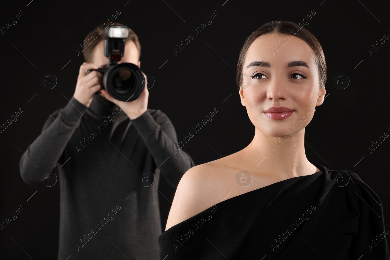 Photo of Photographer taking picture of beautiful woman on black background, selective focus