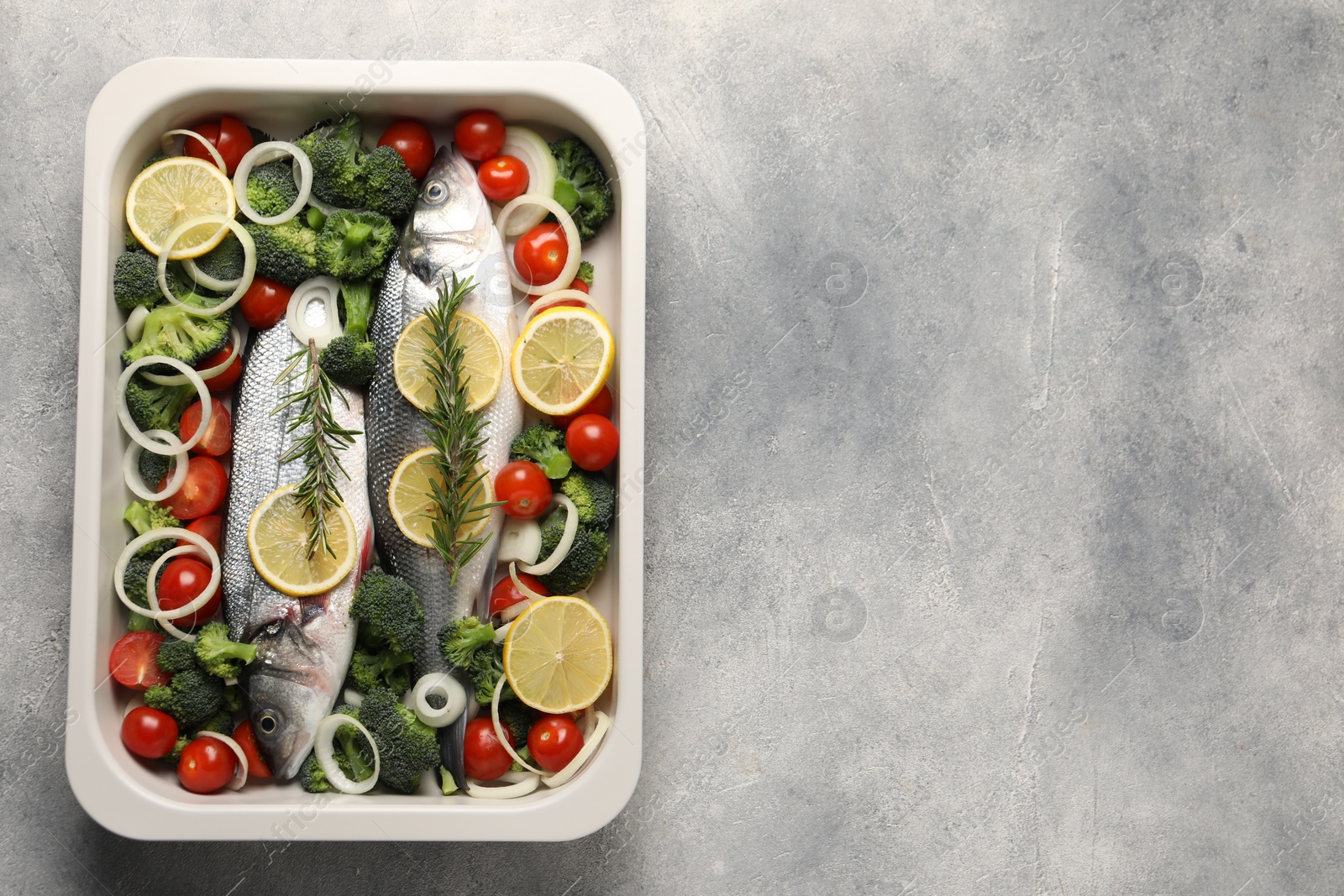 Photo of Raw fish with vegetables and lemon in baking dish on grey textured table, top view. Space for text