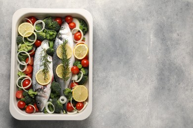 Photo of Raw fish with vegetables and lemon in baking dish on grey textured table, top view. Space for text