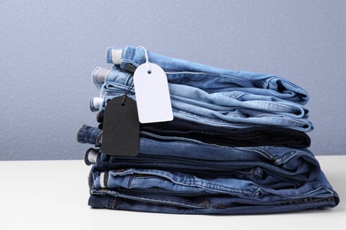 Photo of Stack of stylish jeans with tags on table