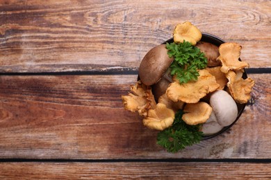 Photo of Bowl of different mushrooms and parsley on wooden table, top view. Space for text