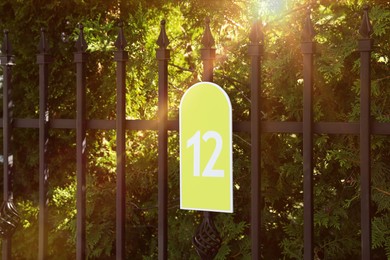 Plate with house number twelve hanging on iron fence outdoors