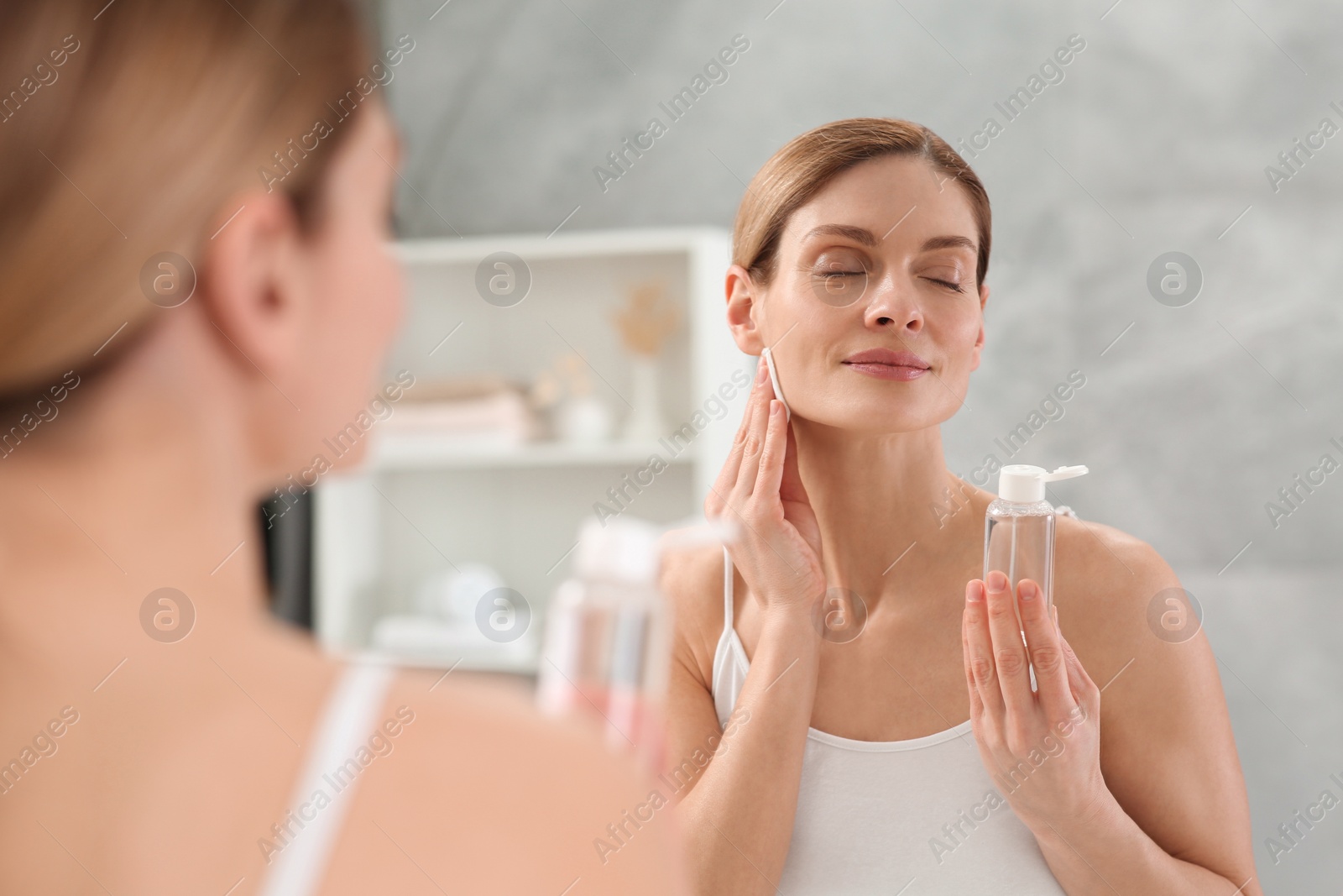 Photo of Beautiful woman removing makeup with cotton pad near mirror indoors