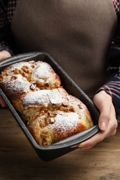 Woman holding baking pan with delicious yeast dough cake at wooden table, closeup