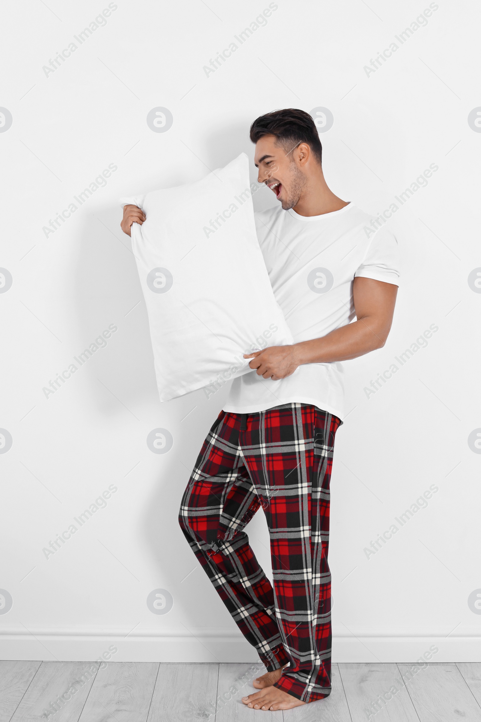 Photo of Young man with soft pillow near white wall