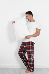 Young man with soft pillow near white wall