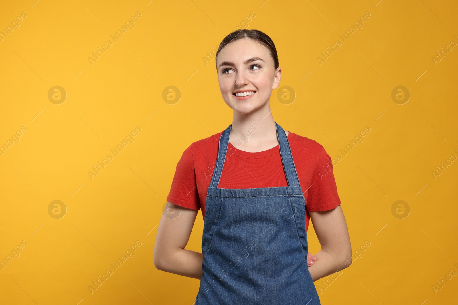 Photo of Beautiful young woman in clean denim apron on orange background