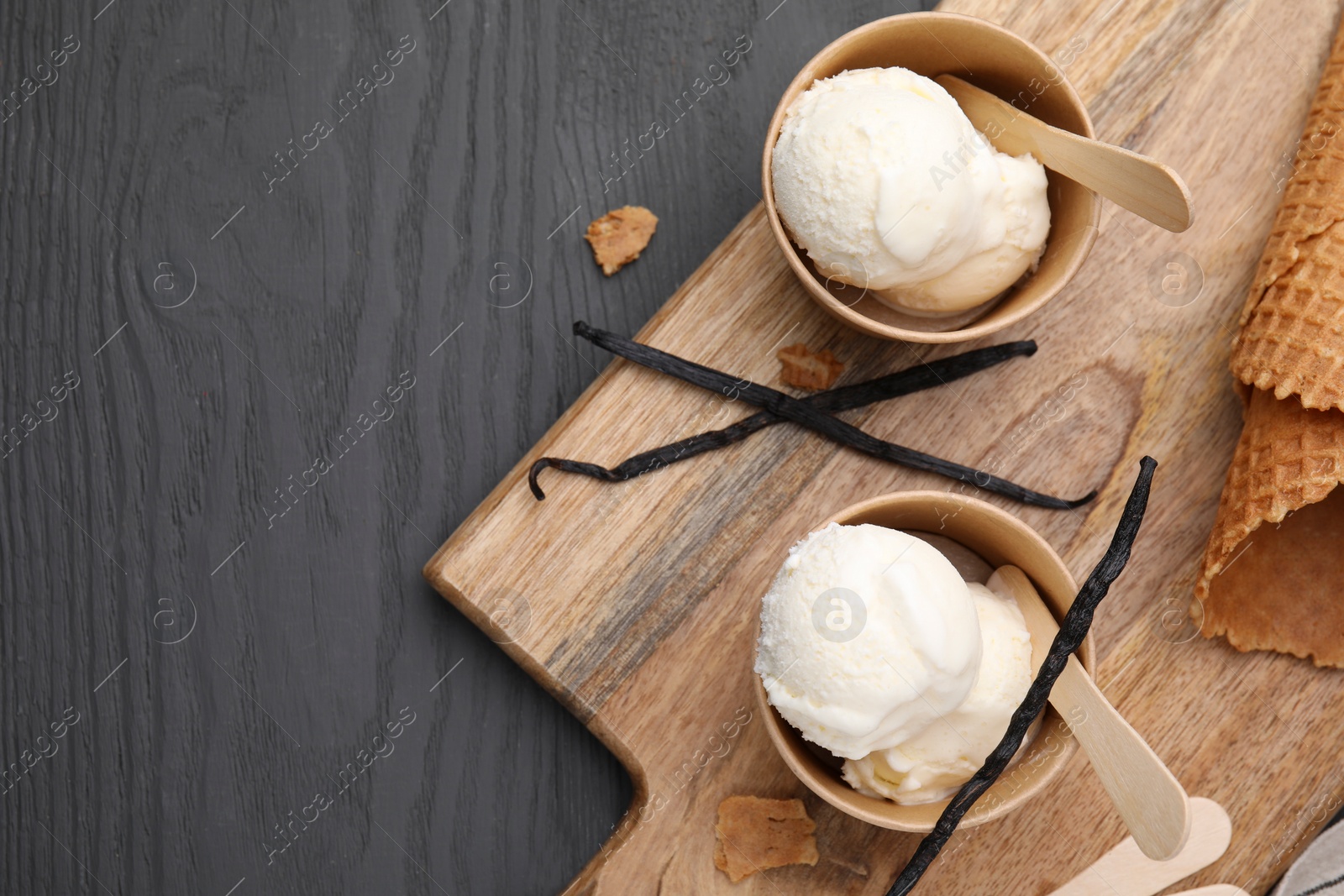 Photo of Paper cups with delicious ice cream and vanilla pods on grey wooden table, flat lay. Space for text