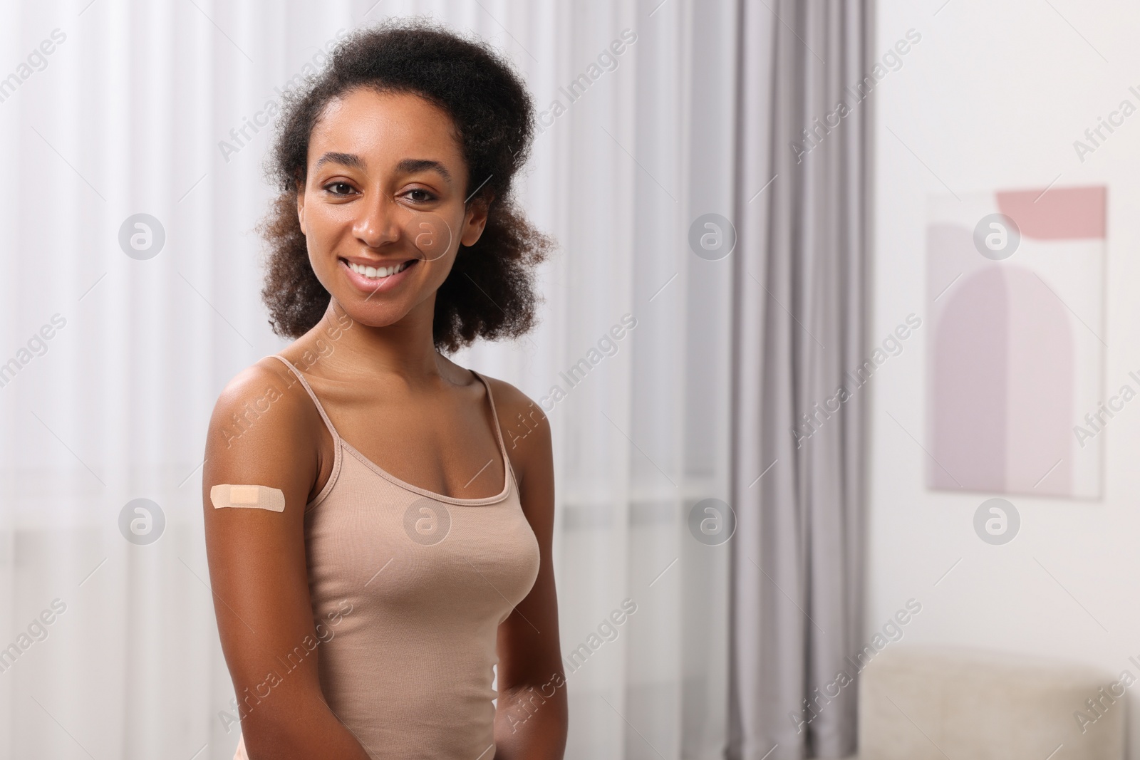 Photo of Happy young woman with adhesive bandage on her arm after vaccination indoors. Space for text