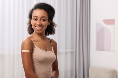 Happy young woman with adhesive bandage on her arm after vaccination indoors. Space for text