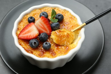 Taking delicious creme brulee with berries and mint from bowl at grey table, closeup