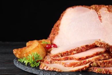 Plate with delicious ham on grey wooden table against black background, closeup