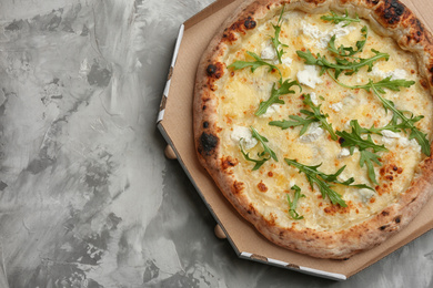 Photo of Delicious cheese pizza with arugula in takeout box on grey table, top view