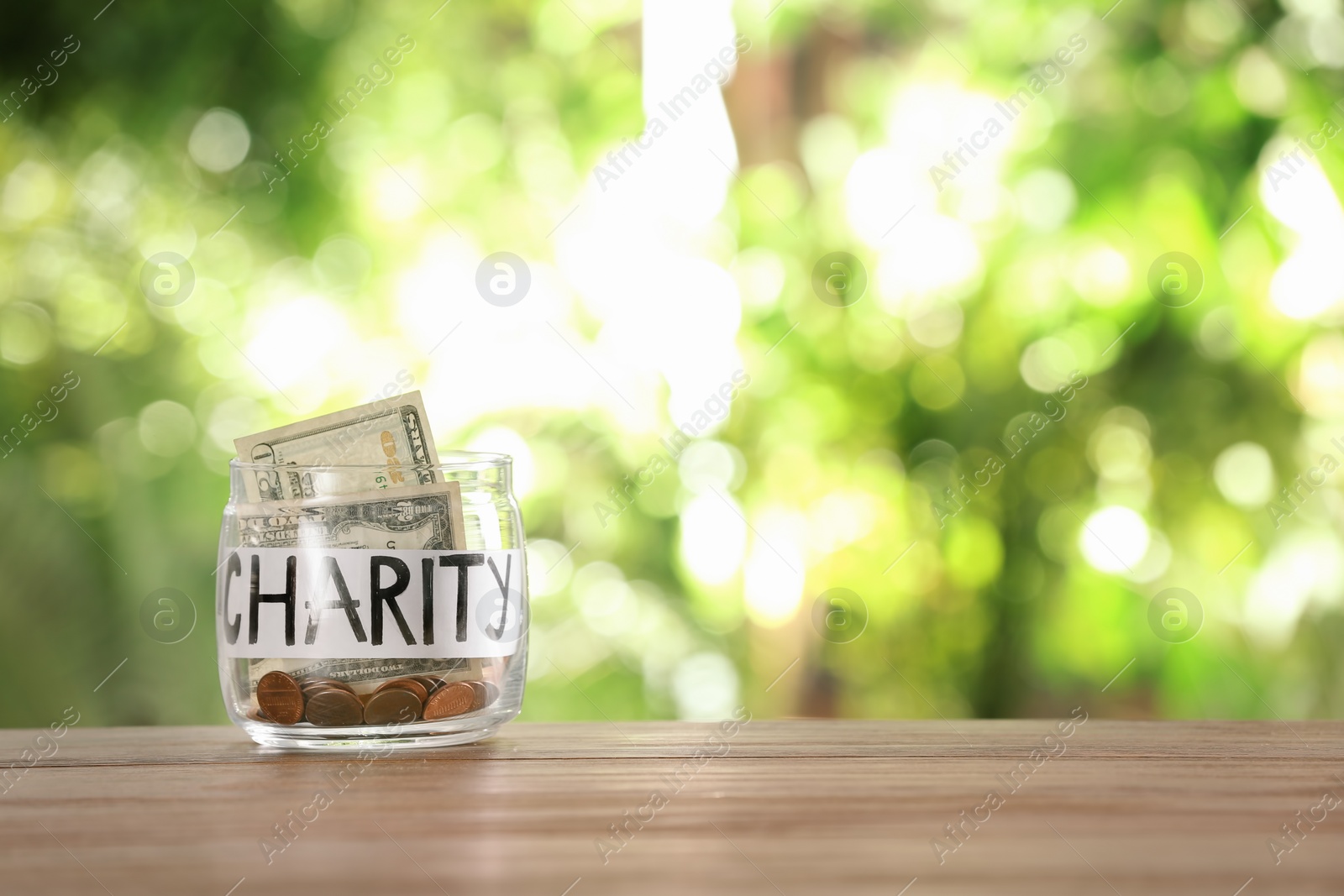 Photo of Glass jar with money and word CHARITY on table against blurred background, space for text