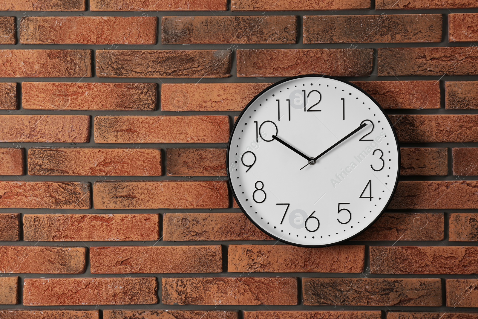 Photo of Stylish analog clock hanging on brick wall. Space for text