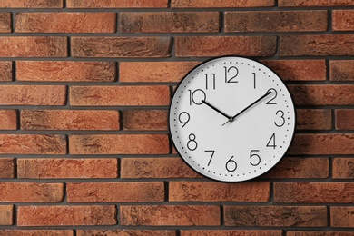 Photo of Stylish analog clock hanging on brick wall. Space for text