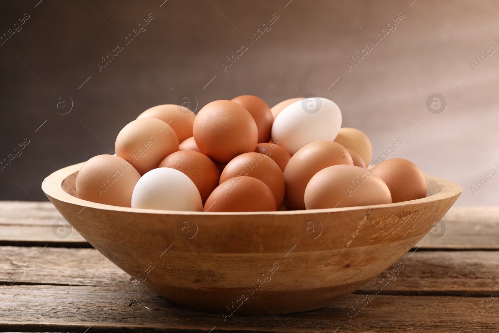 Photo of Chicken eggs in bowl on wooden table, closeup