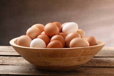 Chicken eggs in bowl on wooden table, closeup