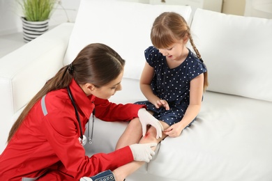 Photo of Nurse examining little girl's leg injury at home. First aid