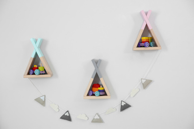 Photo of Wigwam shaped shelves with toys and garland on white wall. Children's room interior design