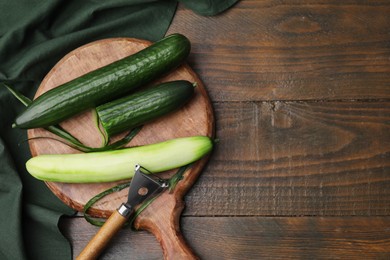 Fresh cucumbers and peeler on wooden table, top view. Space for text