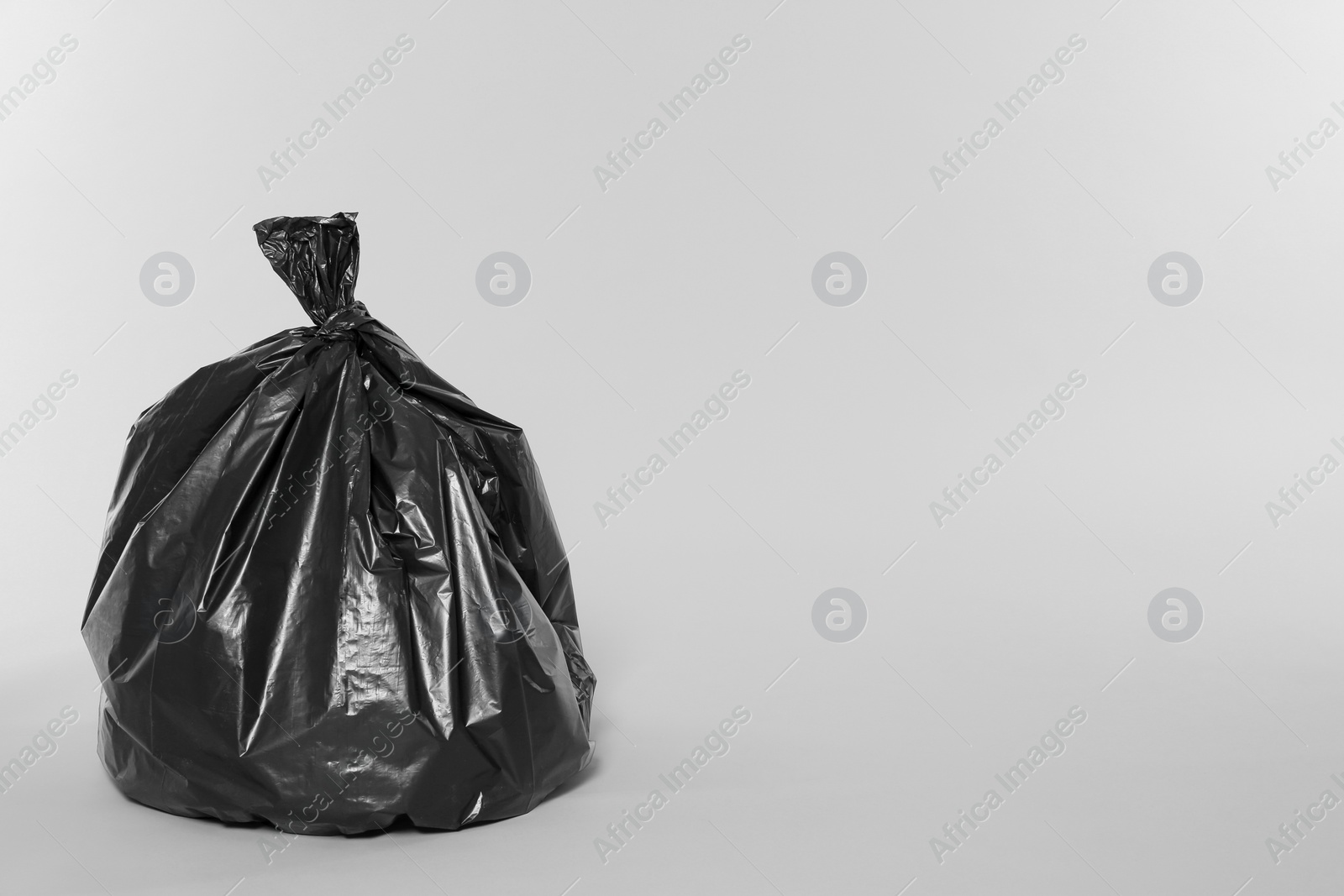 Photo of Trash bag full of garbage on light grey background. Space for text