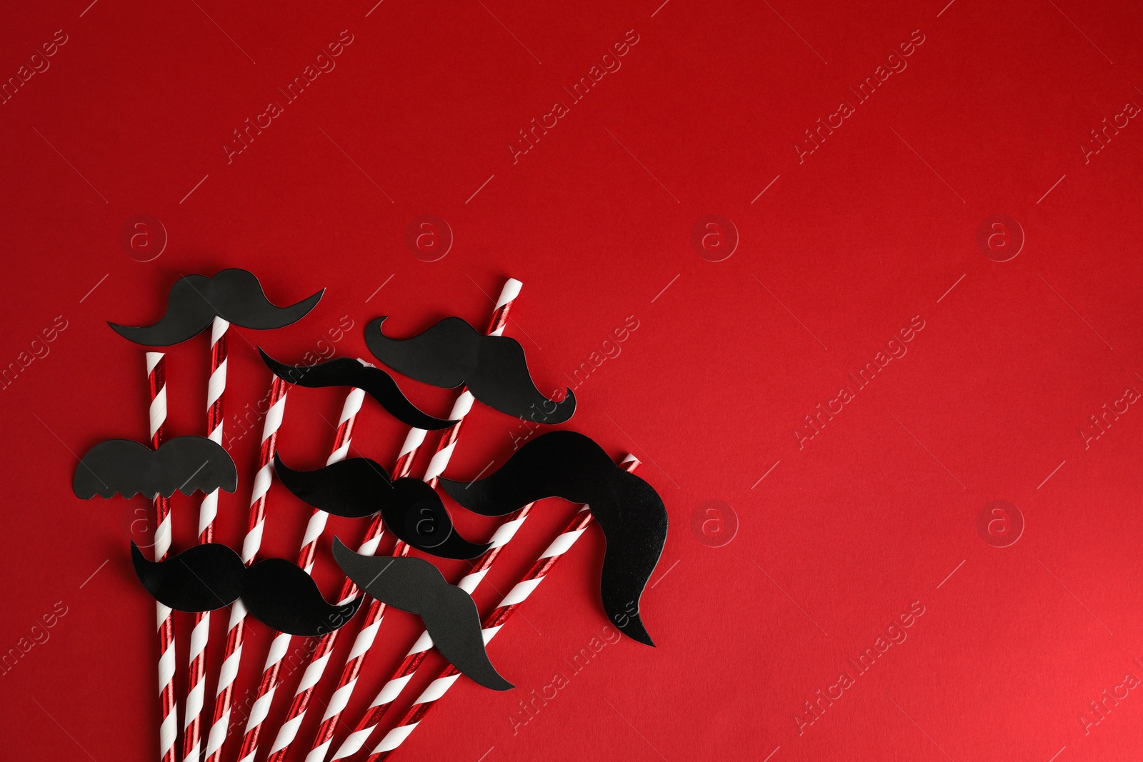 Photo of Fake paper mustaches with party props on red background, flat lay. Space for text
