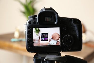 Camera with photo of stylish workplace on screen indoors, selective focus. Fashion blogger