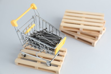 Photo of Metal nails in shopping cart on light grey background, space for text