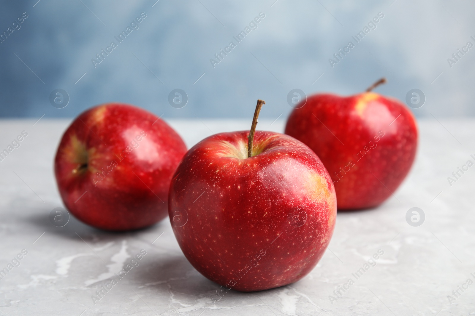 Photo of Ripe juicy red apples on grey table against blue background