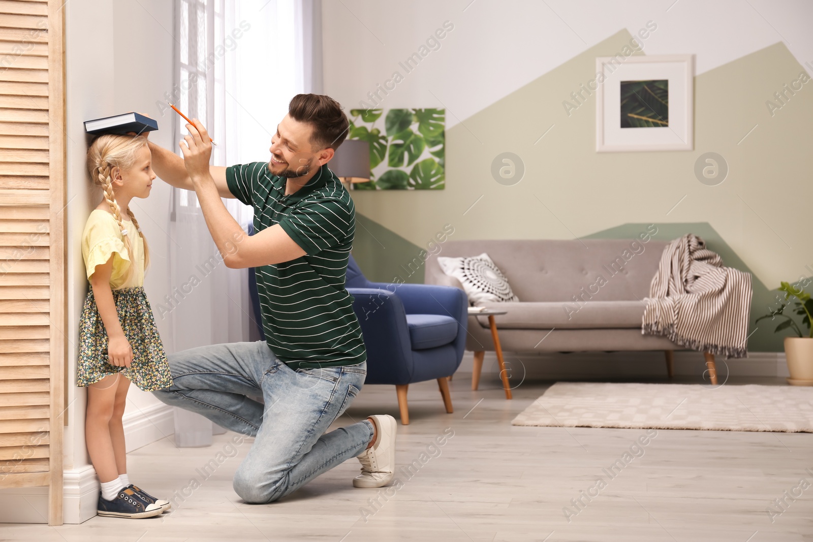 Photo of Young man measuring his daughter's height at home