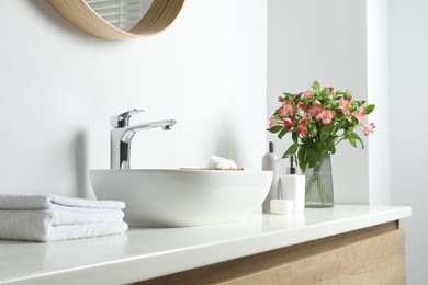 Photo of Vase with beautiful Alstroemeria flowers and toiletries near sink in bathroom