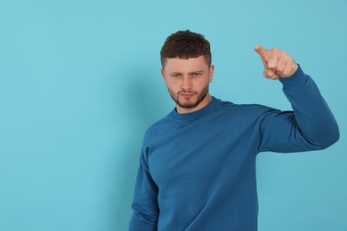 Photo of Aggressive young man pointing on light blue background. Space for text