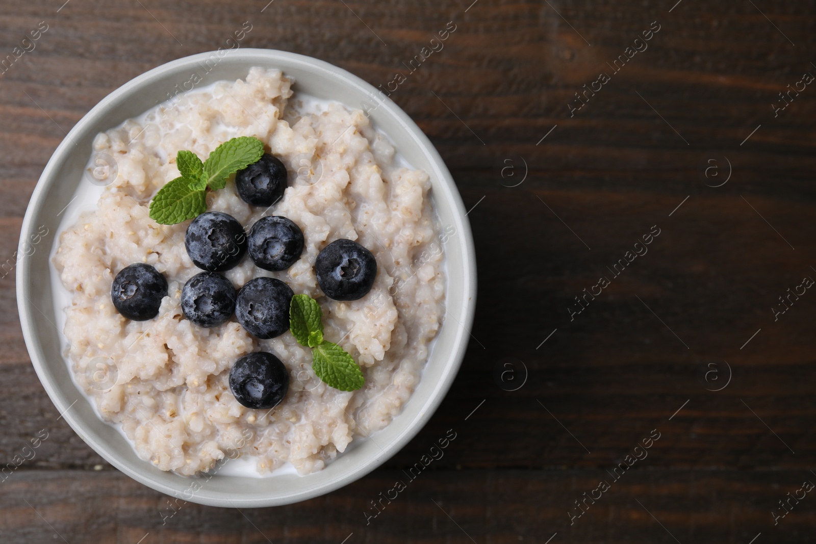 Photo of Delicious barley porridge with blueberries and mint in bowl on wooden table, top view. Space for text