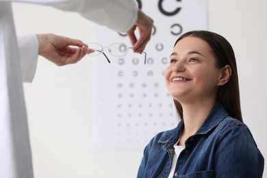 Vision testing. Ophthalmologist giving glasses to young woman indoors