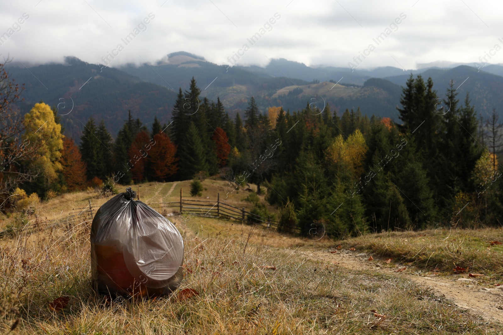 Photo of Trash bag full of garbage on ground against mountain landscape. Space for text