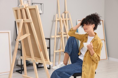 Photo of Young woman with cup near easel in studio