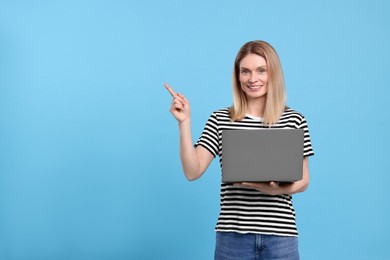 Happy woman with laptop pointing at something on light blue background. Space for text