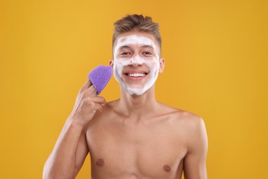 Photo of Happy young man washing his face with sponge on orange background