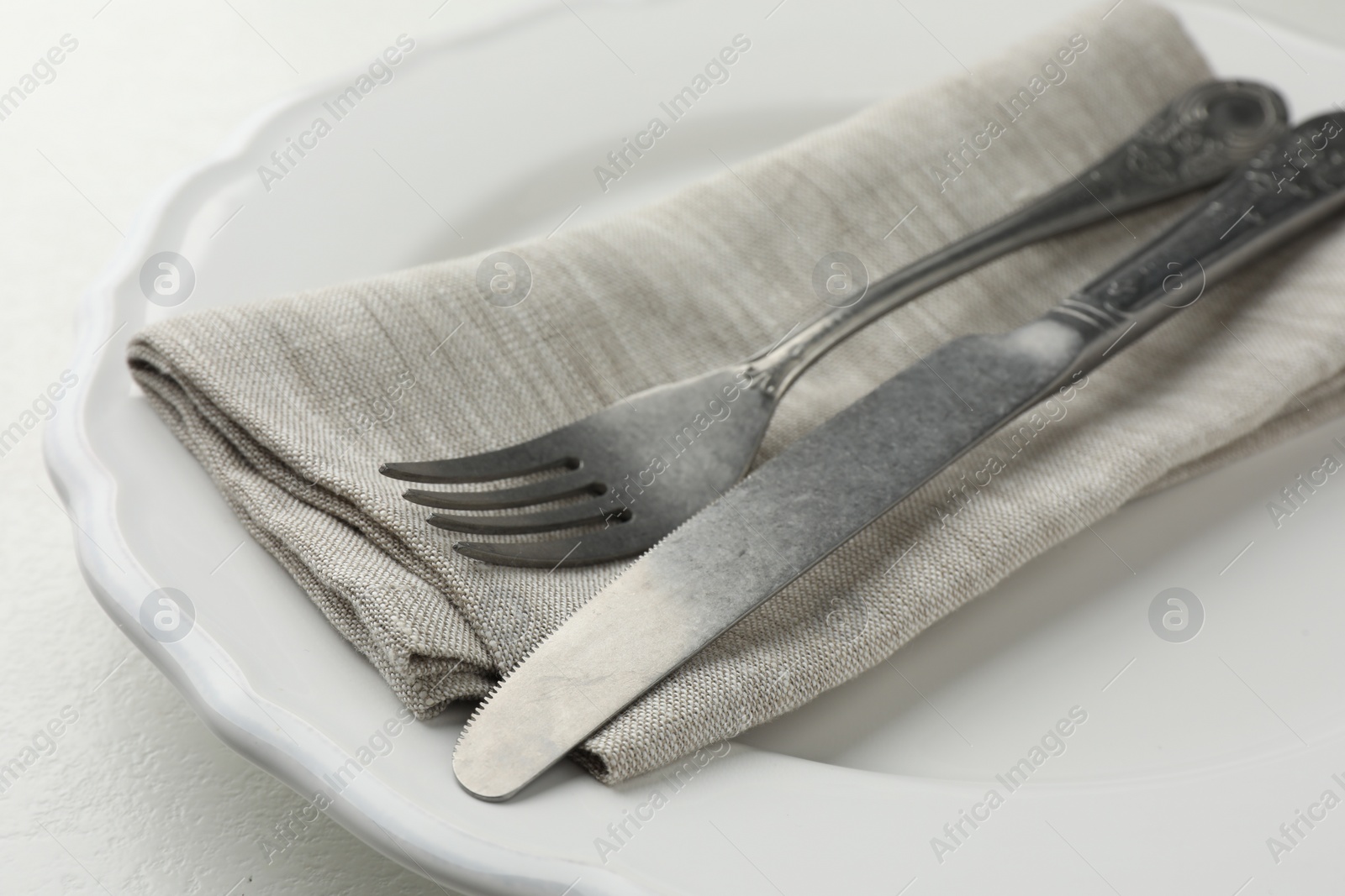 Photo of Stylish setting with cutlery, napkin and plate on white table, closeup