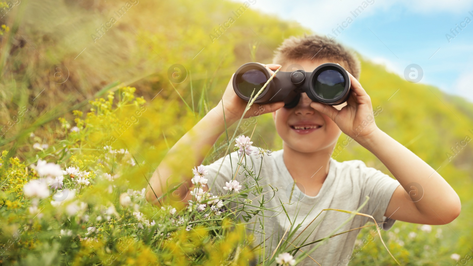 Image of Little boy with binoculars in field on sunny day